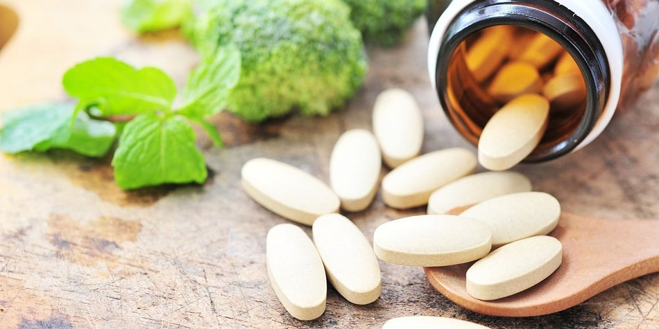 A bottle of large white tablets spills onto a countertop with broccoli in the background.